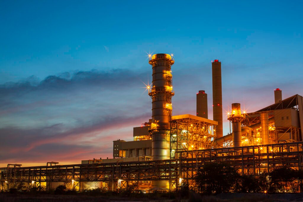Illuminated power plant at twilight with smokestacks and industrial structures, representing onshore industrial security solutions for energy facilities.