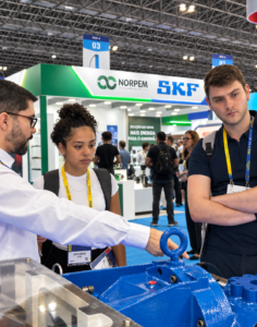 Blue BMS team learning about rotating equipment for offshore operations from an exhibitor at the ROG.e 2026 fair floor in Rio de Janeiro